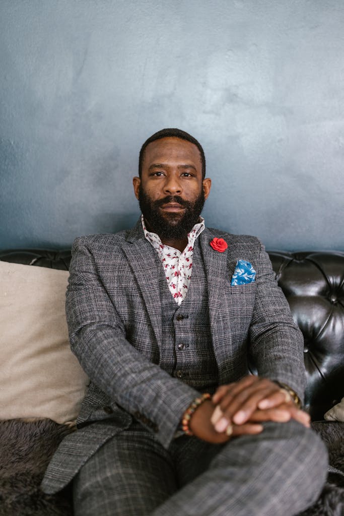 Adult businessman sitting confidently on a black leather couch wearing a tailored gray suit.