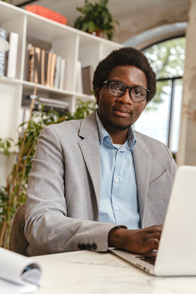 Confident professional man in glasses working on a laptop in a modern office setting.